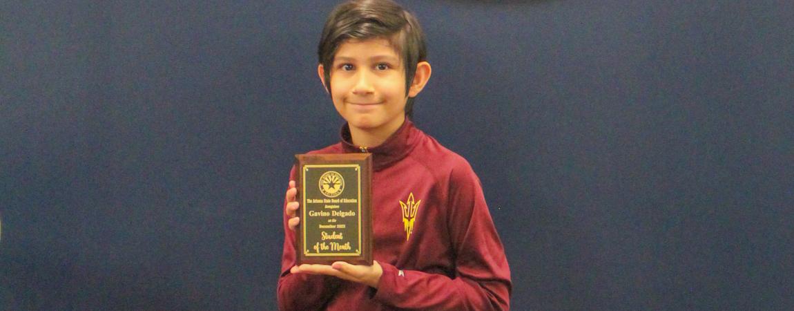 Gavino Delgado, one of the October students of the month holding his award and standing in front of the Arizona State seal