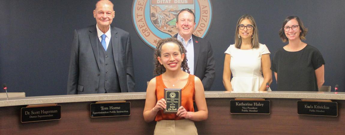Eva Luz Pombo, one of the October students of the month holding her award and standing with the Board Members