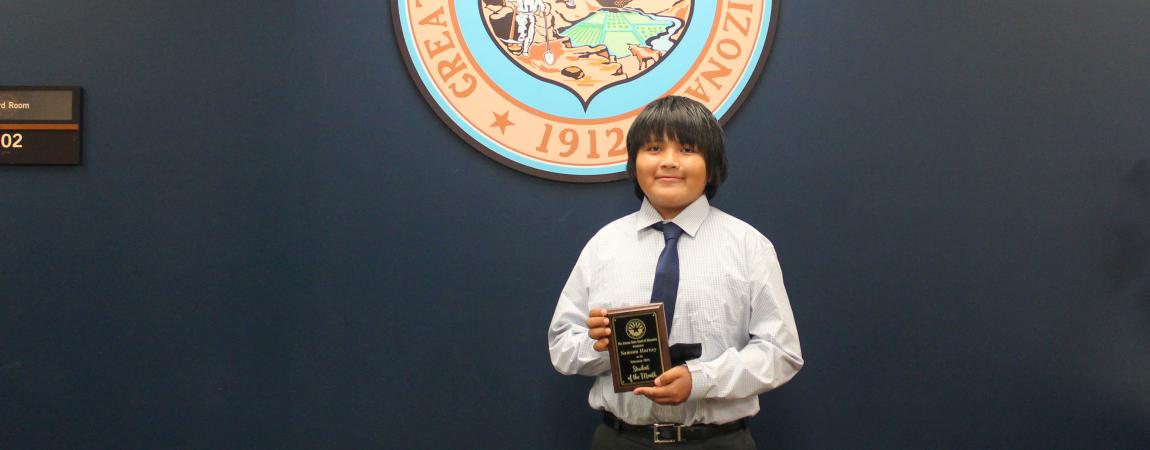 Samson Harney, one of the February 2025 students of the month holding his award and standing in front of the Arizona State seal